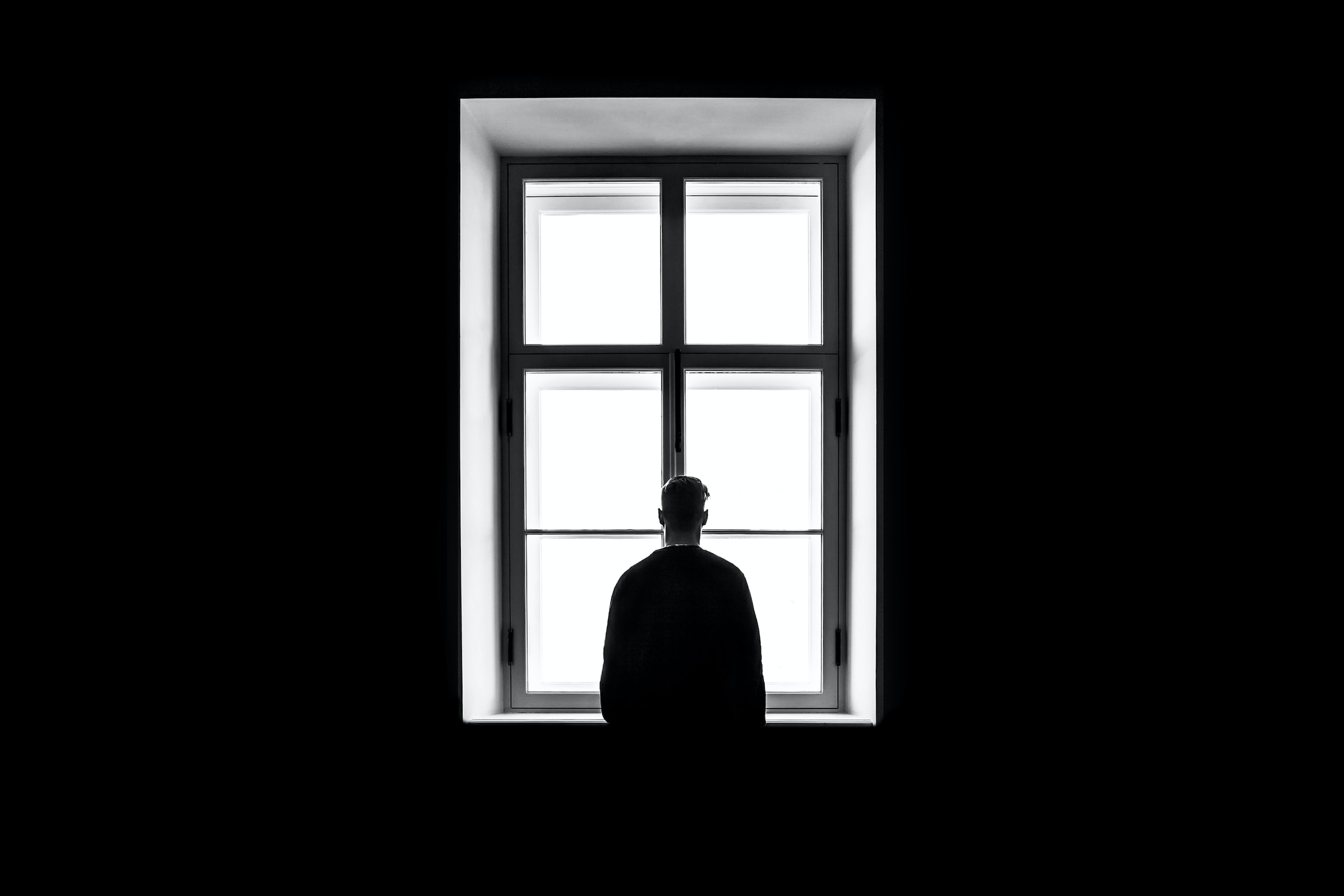 Człowiek stoi przy oknie; okno czarno białe